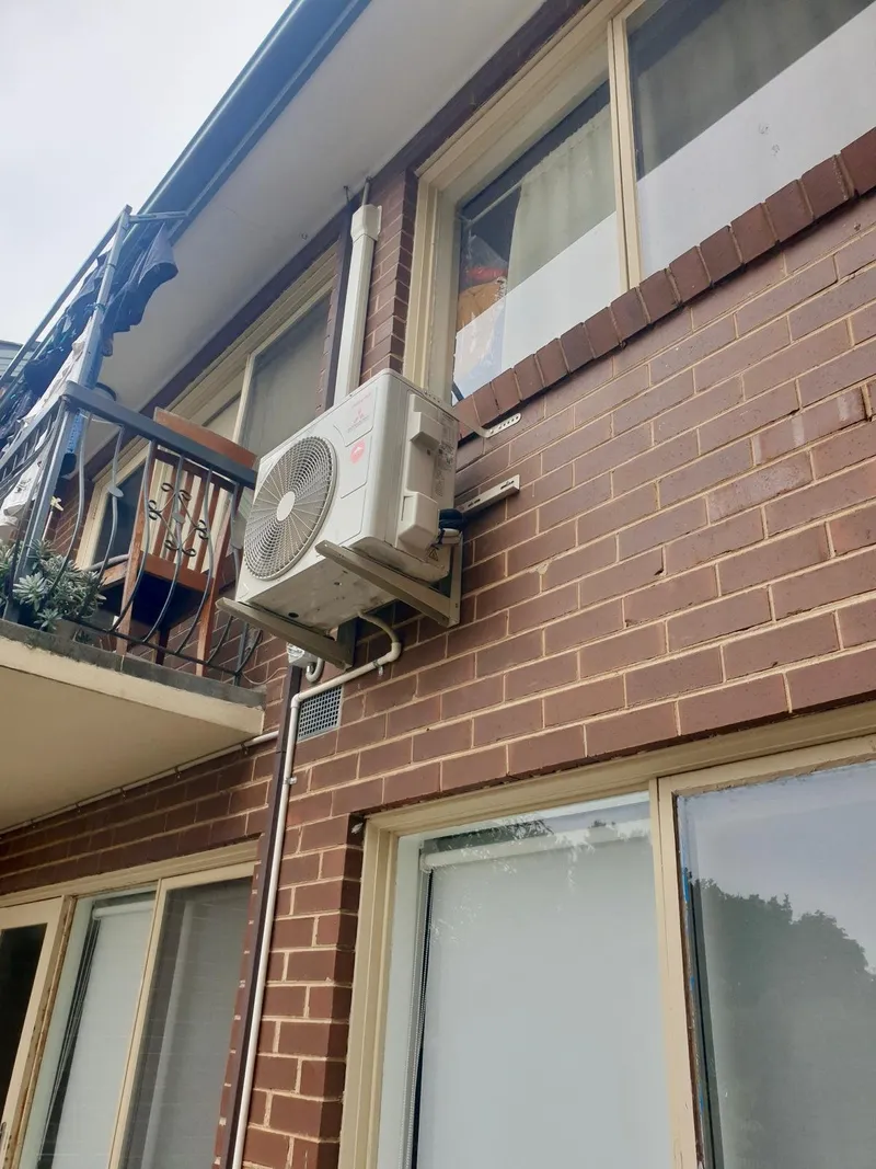 Outdoor unit on a wall bracket beside the balcony of a brick apartment block