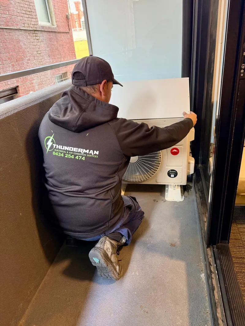 Yiannis kneeling to install an outdoor unit on an apartment balcony