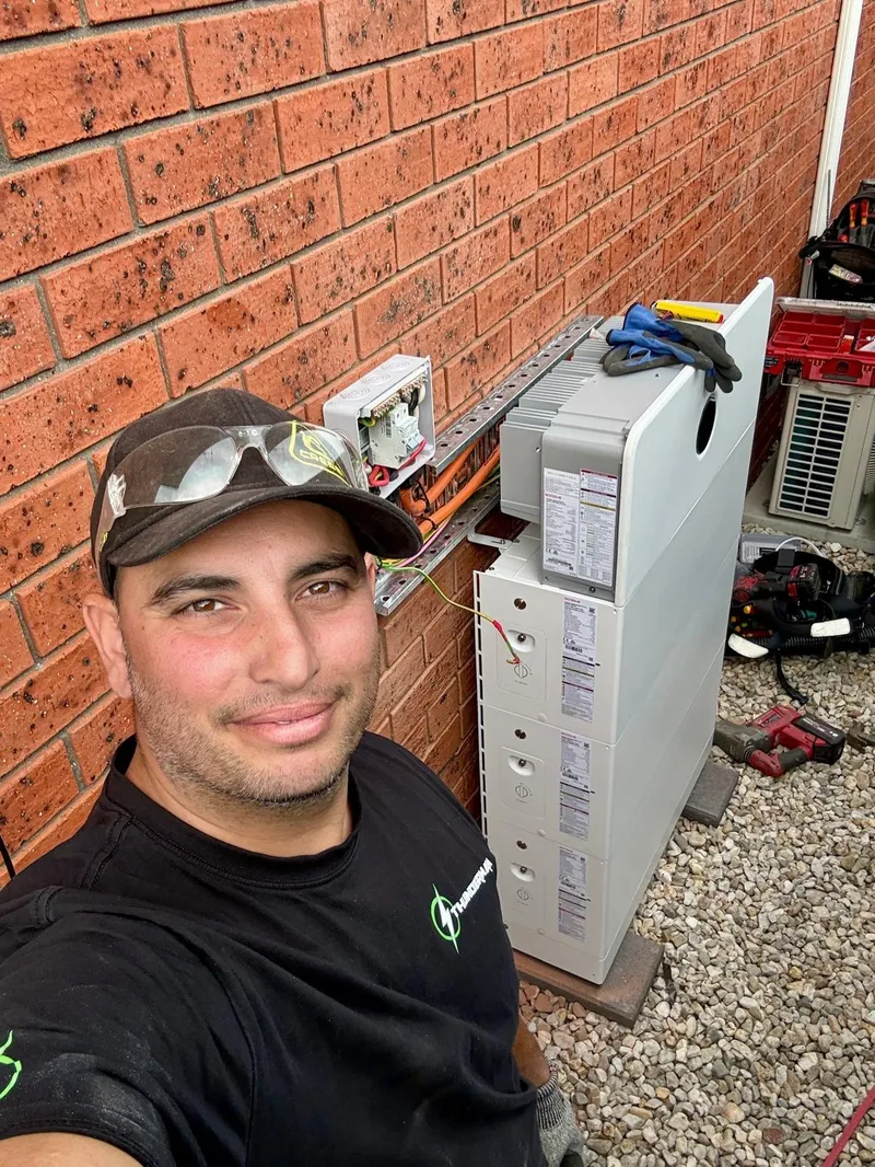 Yiannis taking a selfie beside a newly installed stacked home battery, tools on the gravel