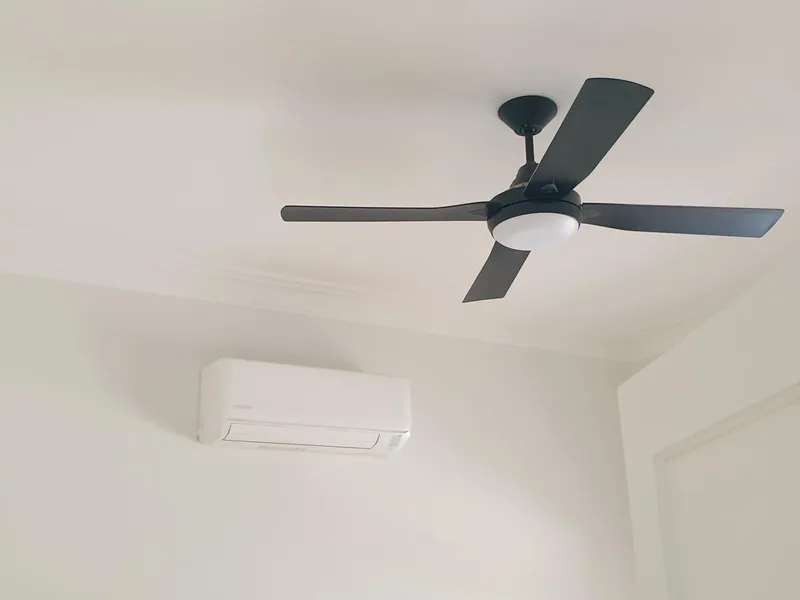 Black ceiling fan with a light, above a wall-mounted split system