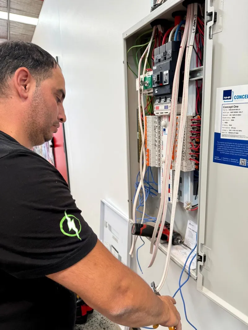 Yiannis working inside an open distribution board full of circuit breakers and cabling