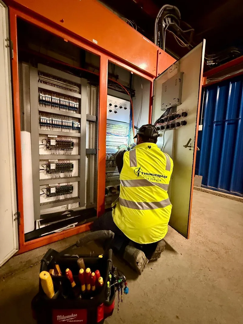 Yiannis in a Thunderman hi-vis vest kneeling to work inside an orange control cabinet