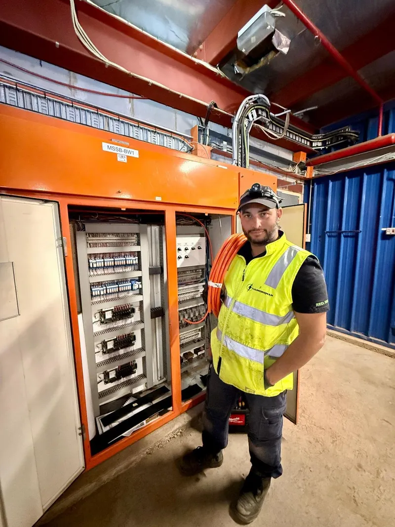 Yiannis in a hi-vis vest beside a large open orange control cabinet