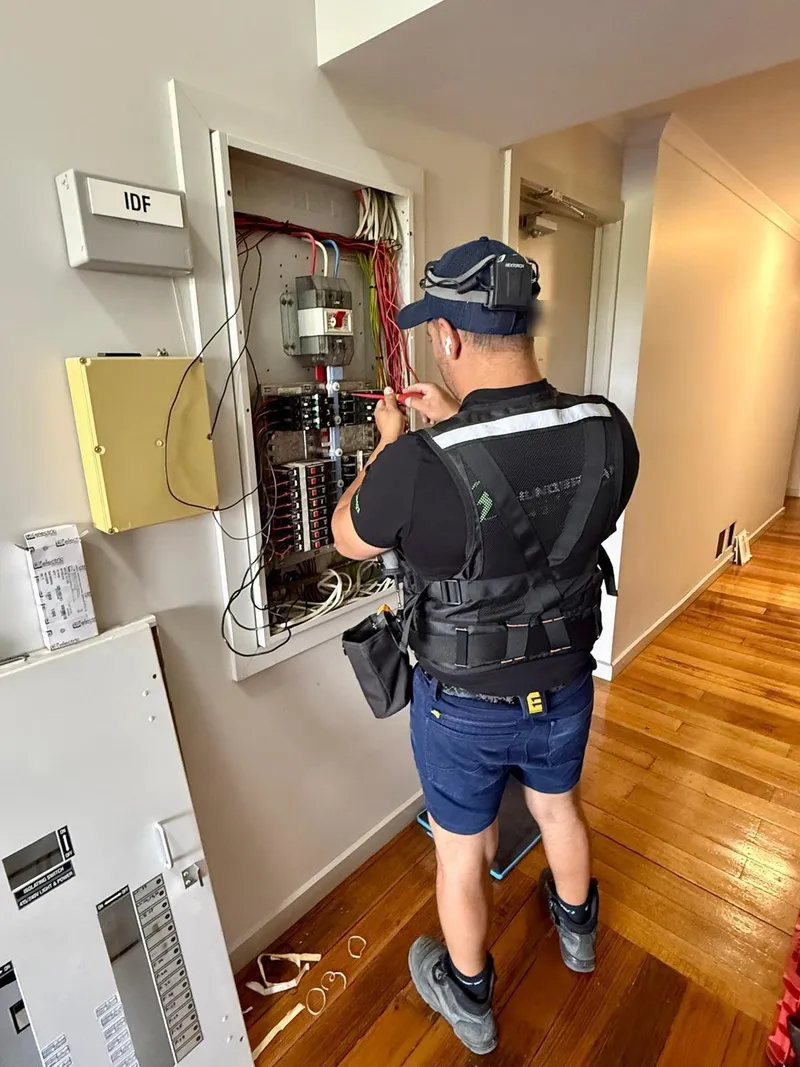 Yiannis in a work vest wiring an open distribution board in a hallway