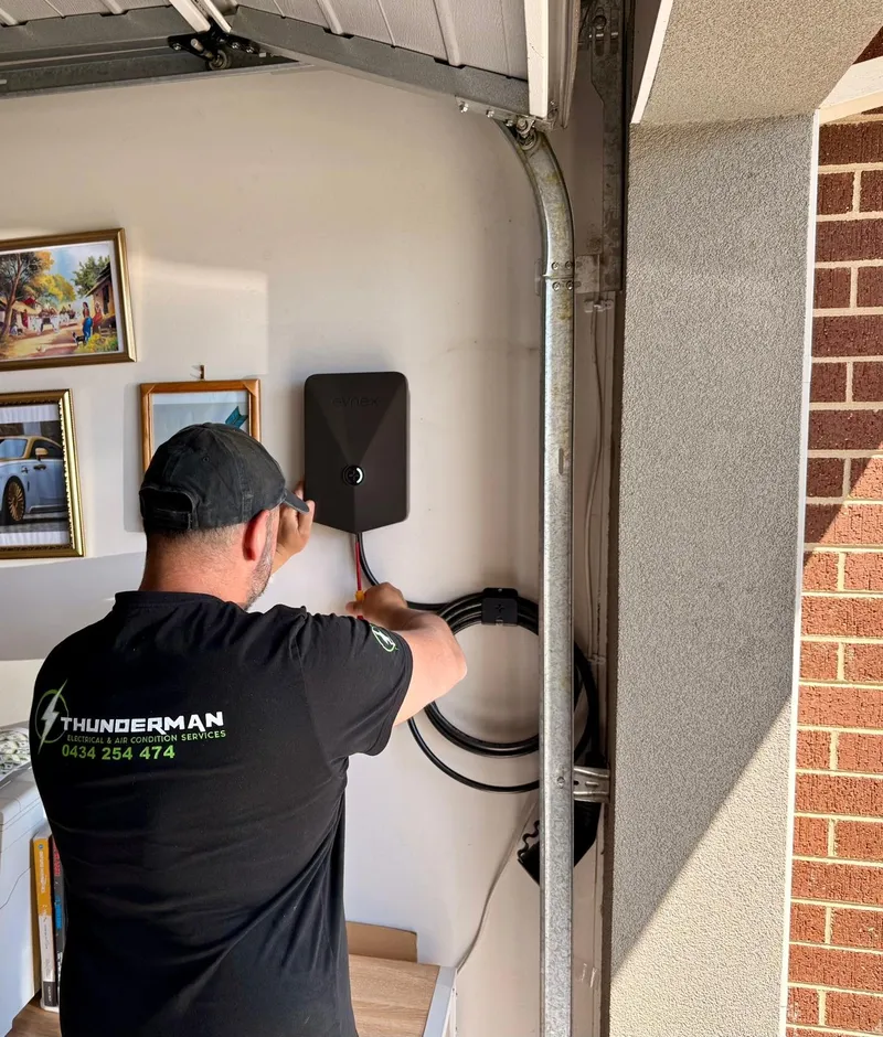 Yiannis mounting a black EV charger on a garage wall