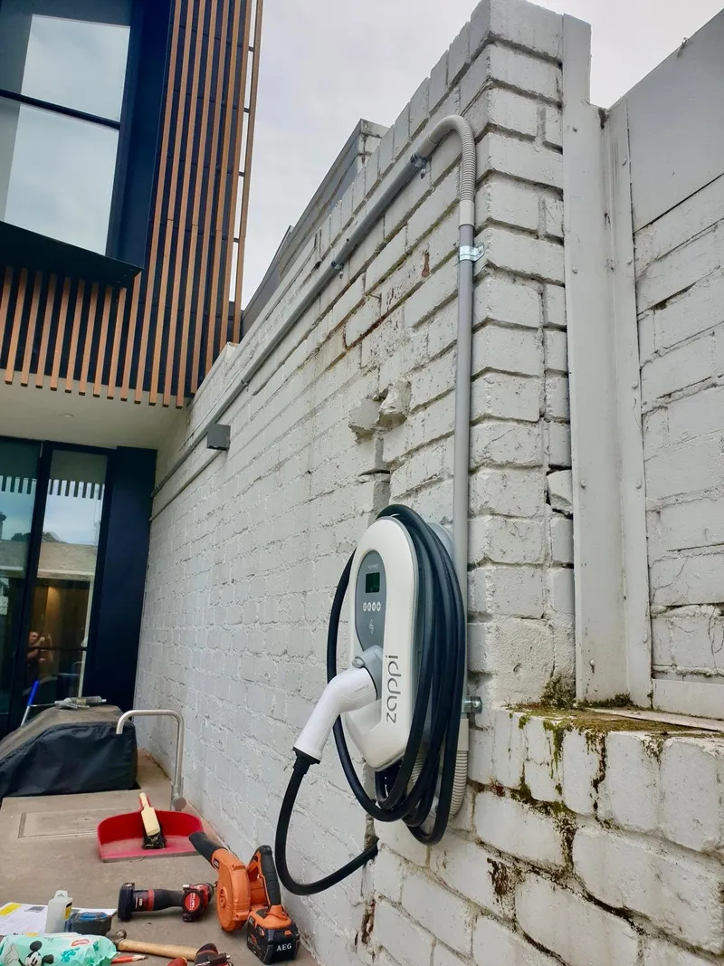 Zappi EV charger with its cable coiled, mounted on a painted brick wall