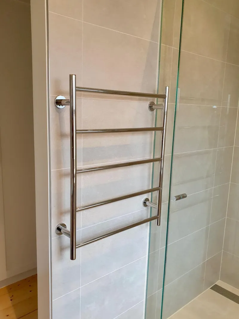 Chrome heated towel rail on a tiled bathroom wall beside a glass shower screen