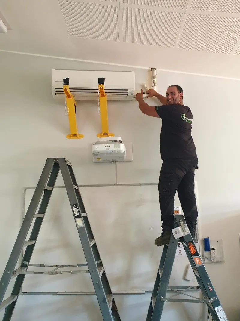 Yiannis on a stepladder mounting a split system indoor unit on support brackets