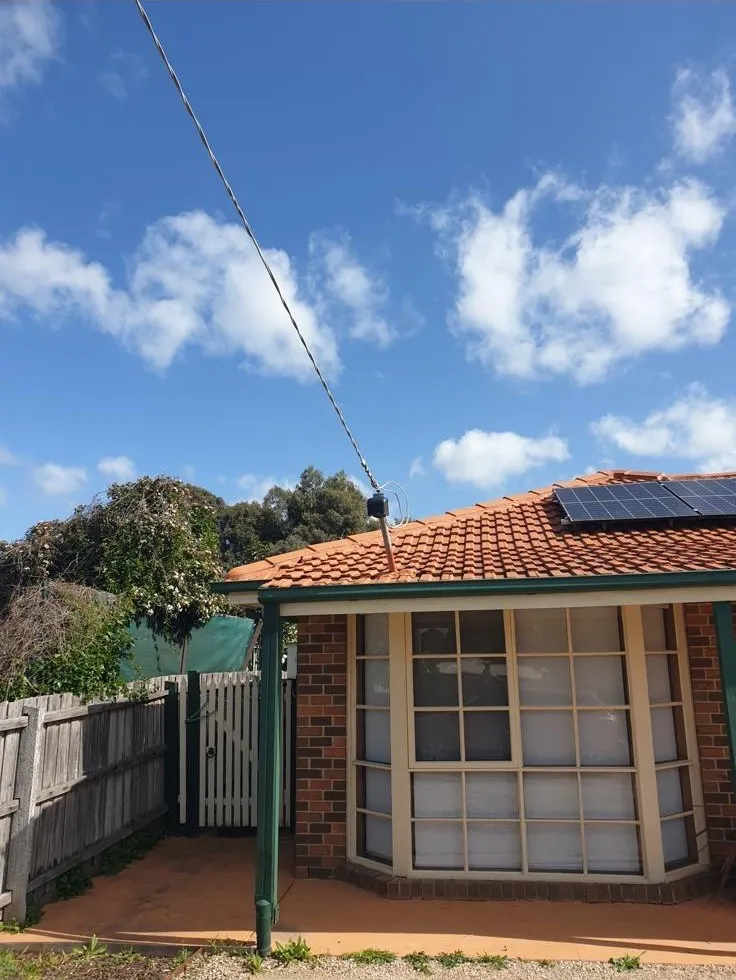 Before: the overhead power line fixed low at the edge of the tiled roof of a brick home