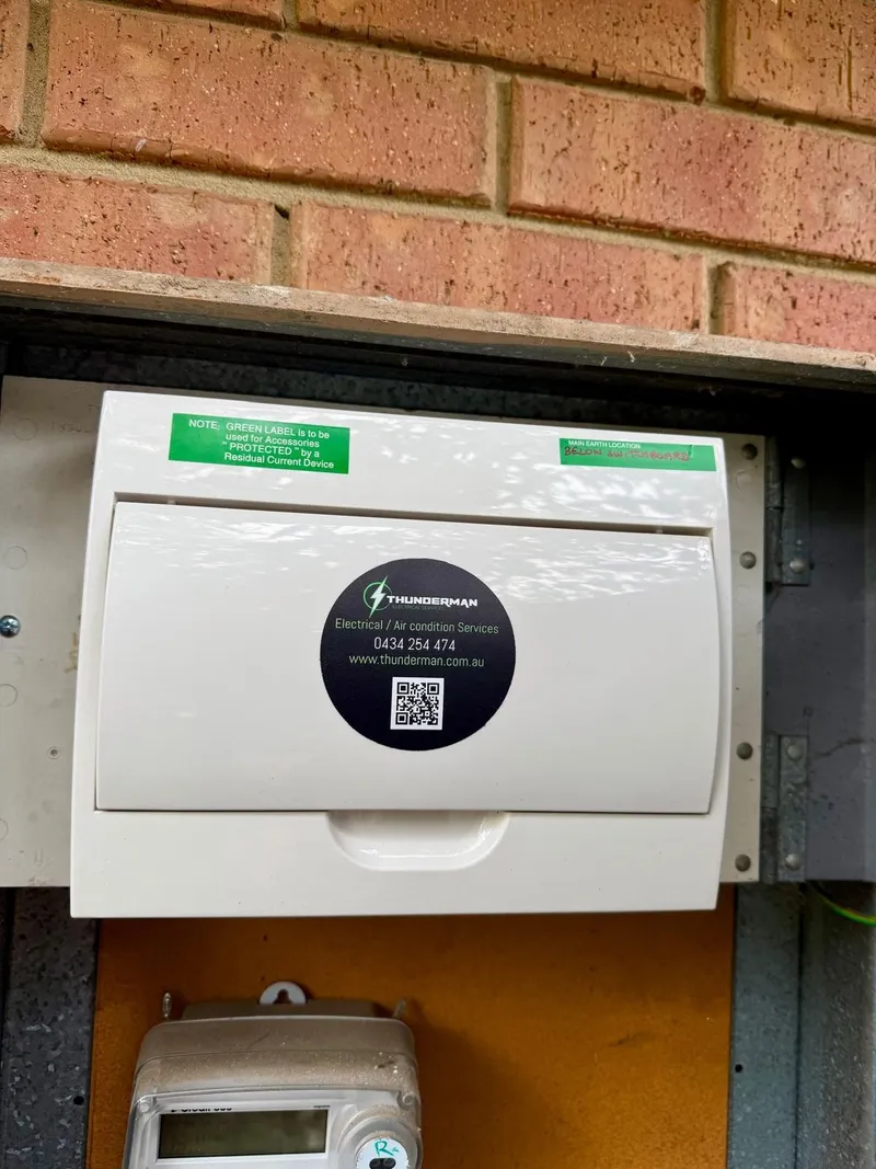 Switchboard cover with green notice labels and a Thunderman sticker, above the meter