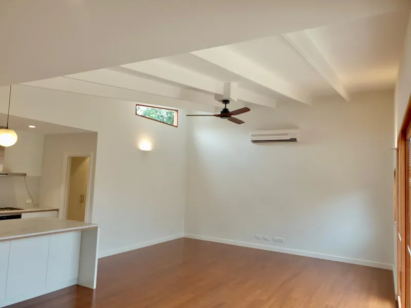 Open-plan living area with a ceiling fan, a wall light, a split system and timber floors