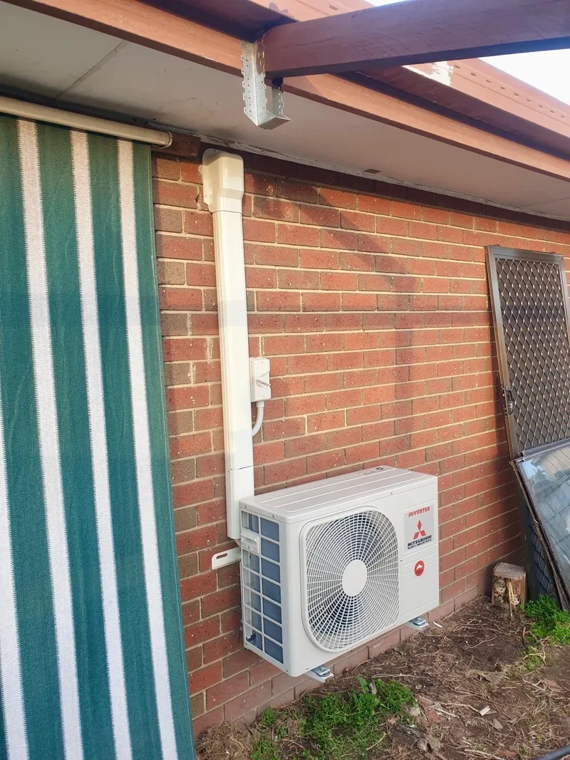 Mitsubishi Heavy Industries outdoor unit on a brick wall, with covered pipework from the eave