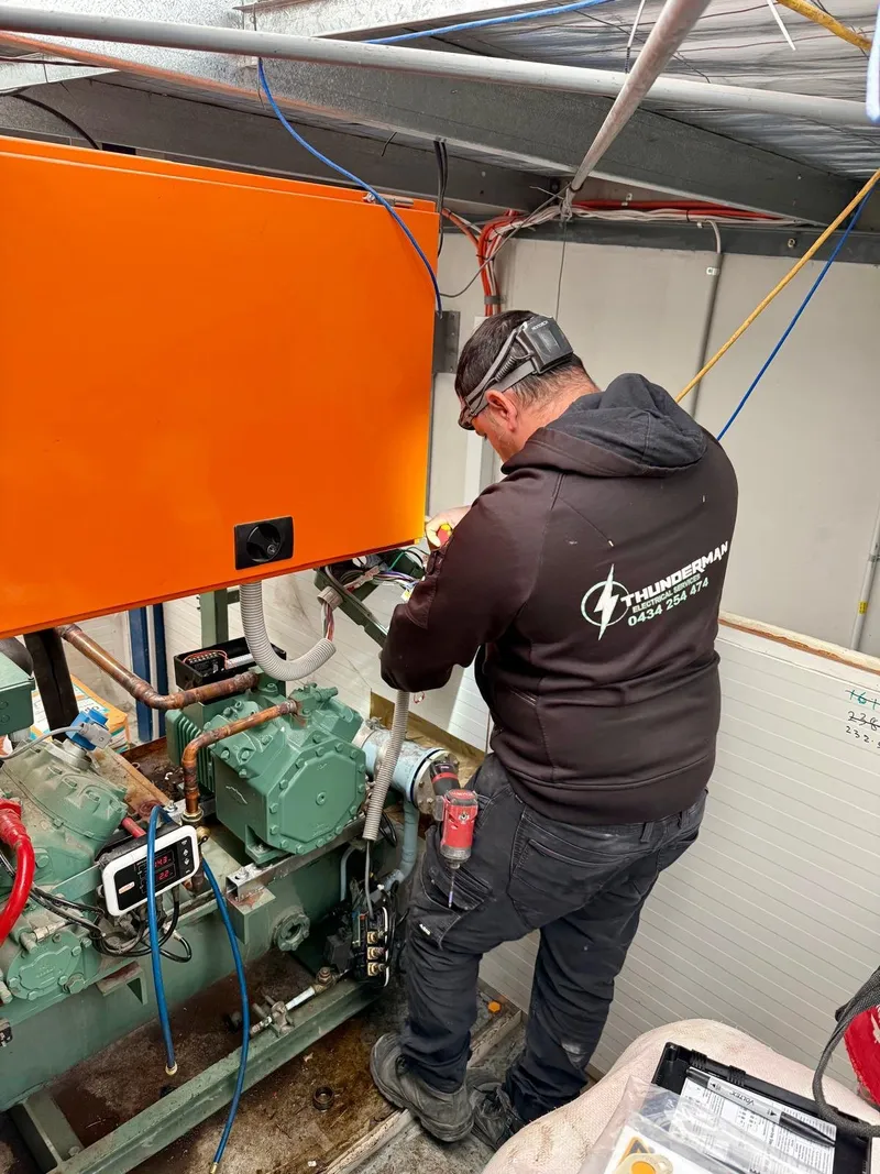 Yiannis working on a refrigeration compressor below an orange control panel