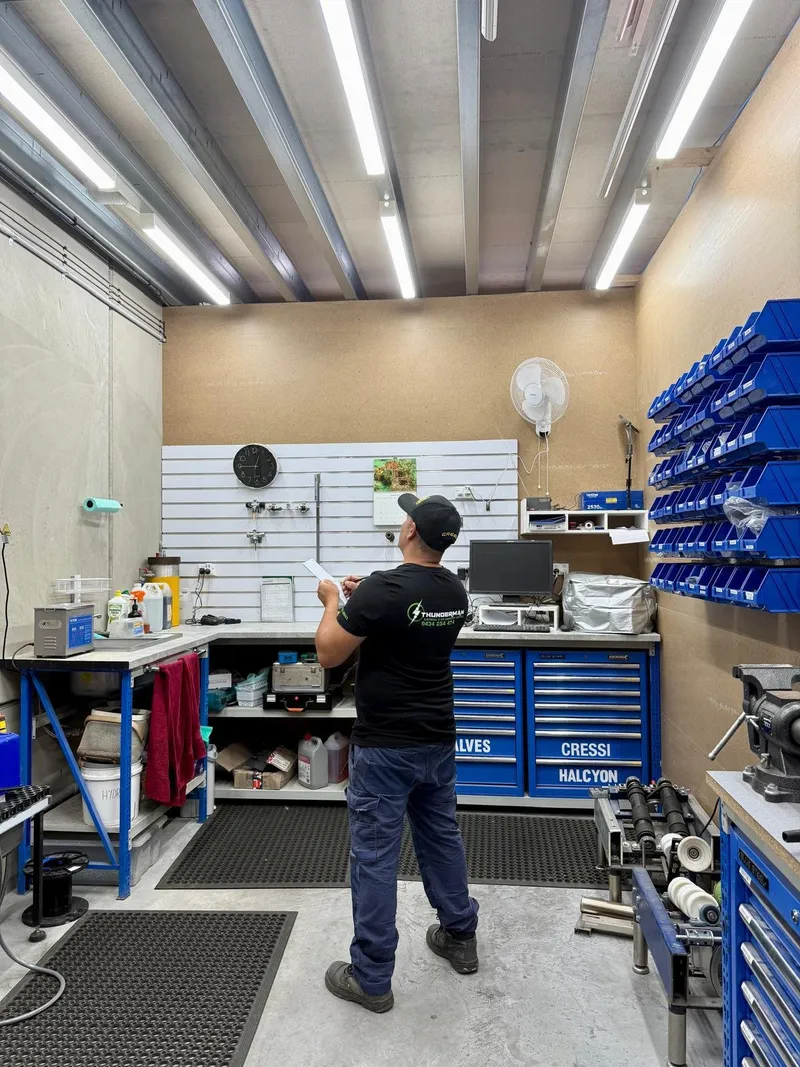 Yiannis holding paperwork in a fitted-out service workshop lit by LED battens