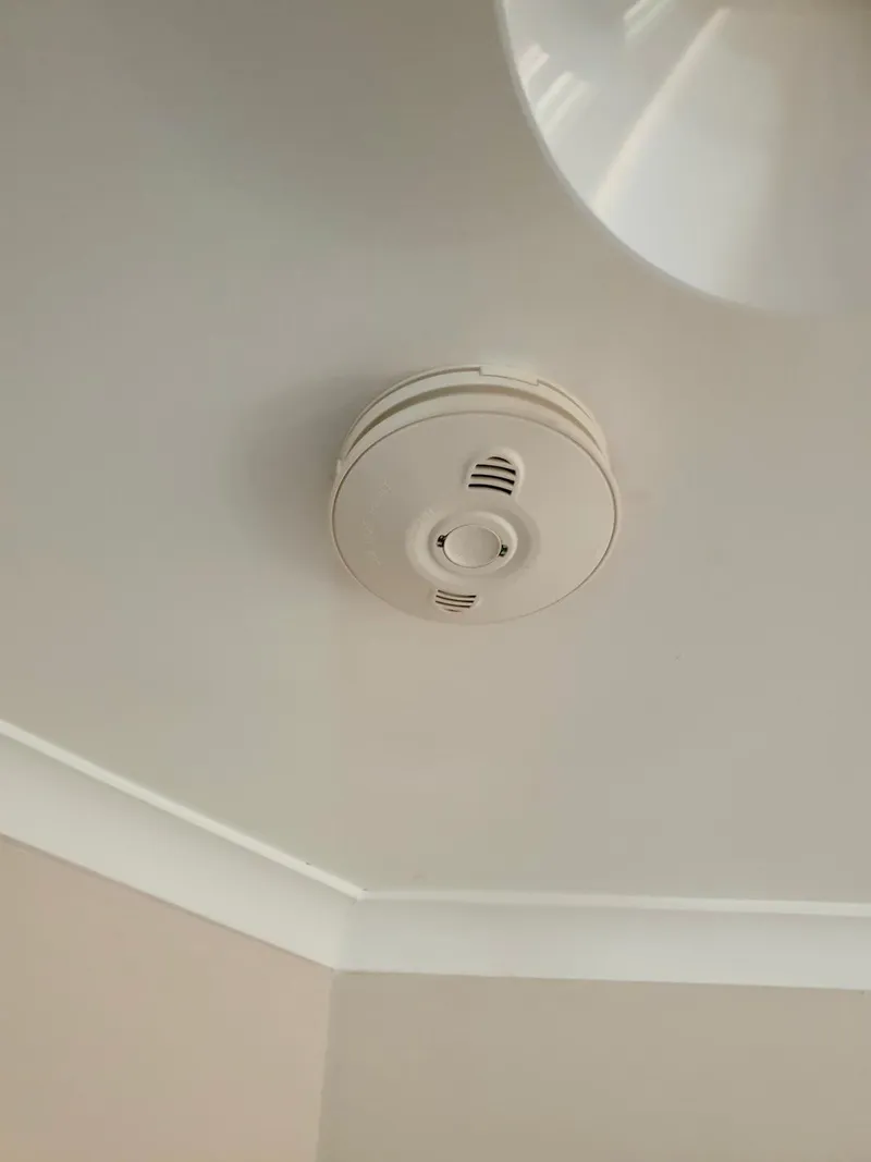 Smoke alarm fitted to a ceiling near the cornice