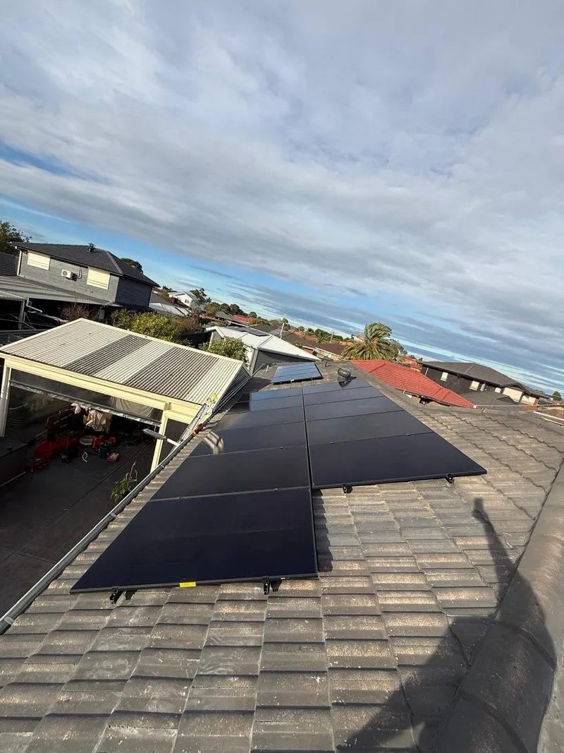 Black solar panels on a grey tiled roof beside a carport, seen from the roof