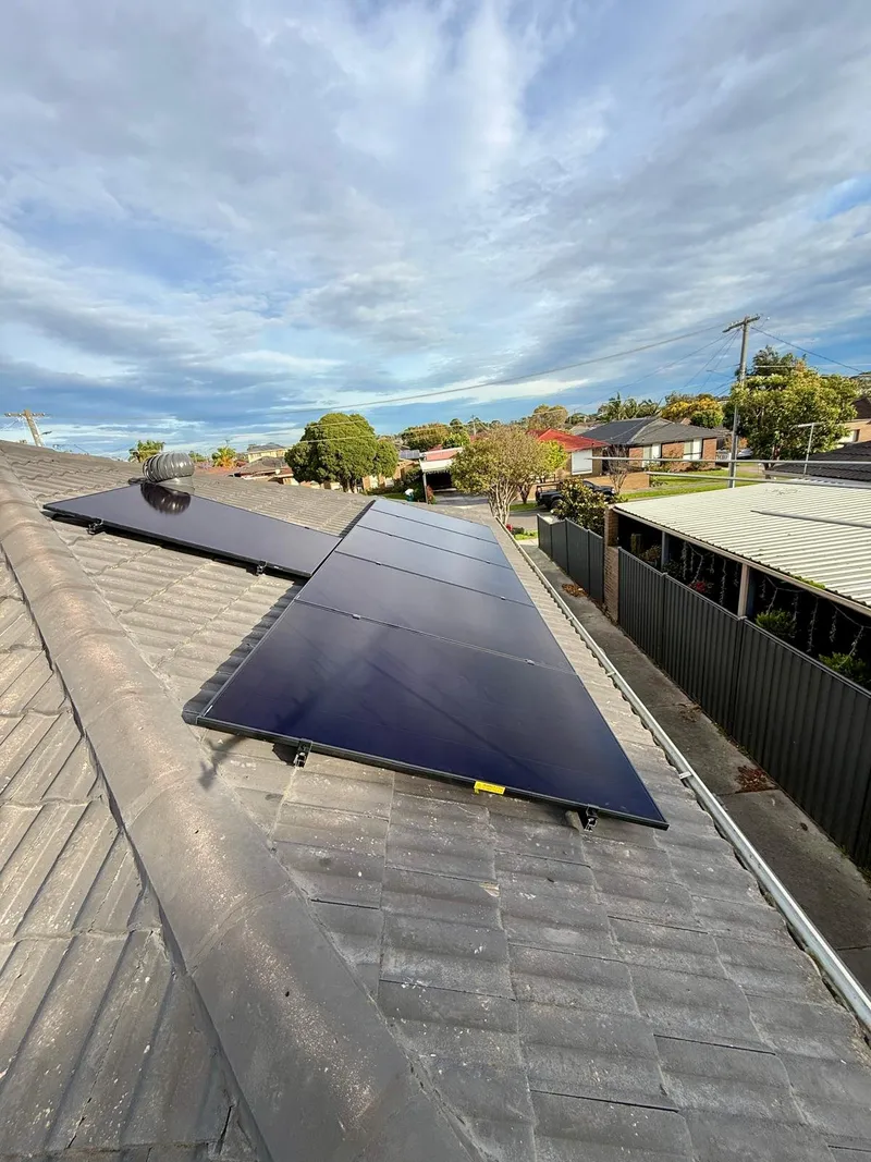 Row of black solar panels on a grey tiled roof, with suburban houses behind