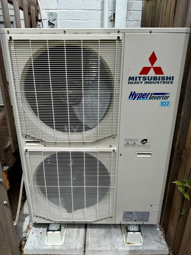 Large Mitsubishi Heavy Industries Hyper Inverter outdoor unit with two fans, on concrete pads