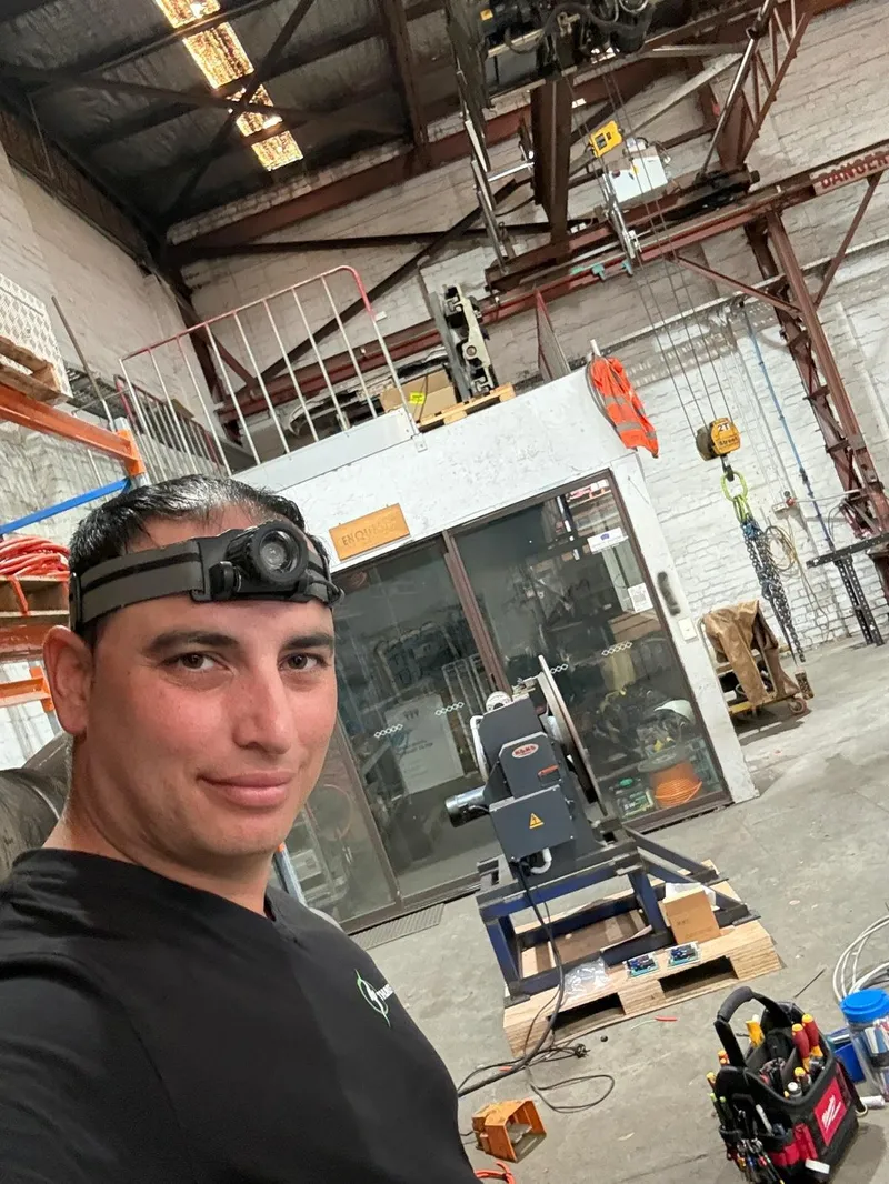 Yiannis wearing a head torch, taking a selfie inside a large industrial workshop