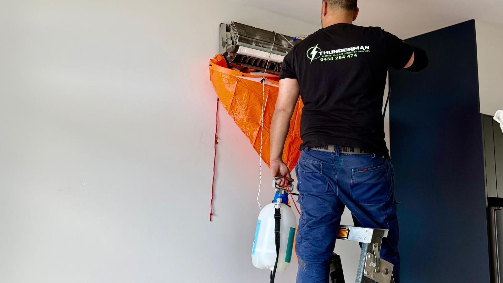 Yiannis on a ladder cleaning a wall-mounted split system with a drain bag fitted
