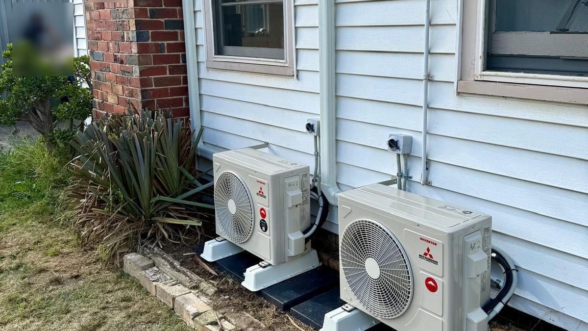 Two Mitsubishi outdoor units on stands beside a weatherboard home