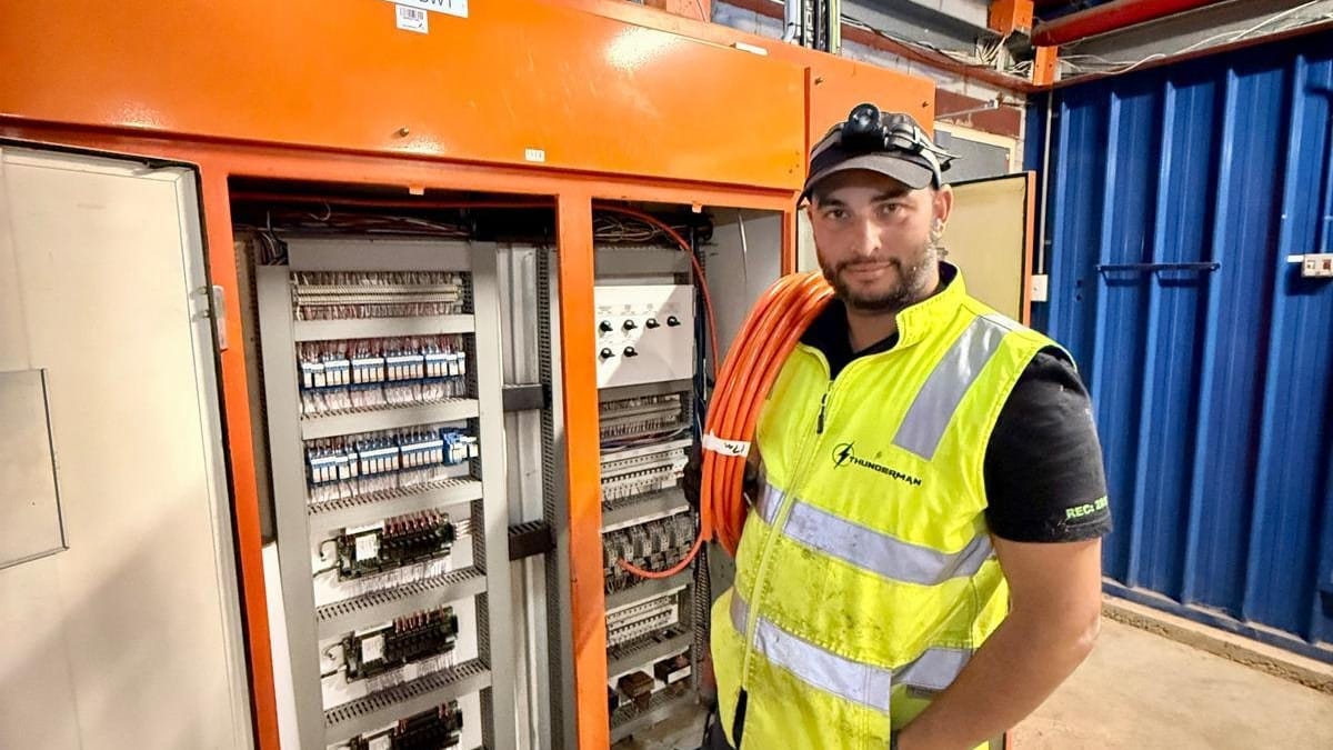 Yiannis in a hi-vis vest beside a large open orange control cabinet