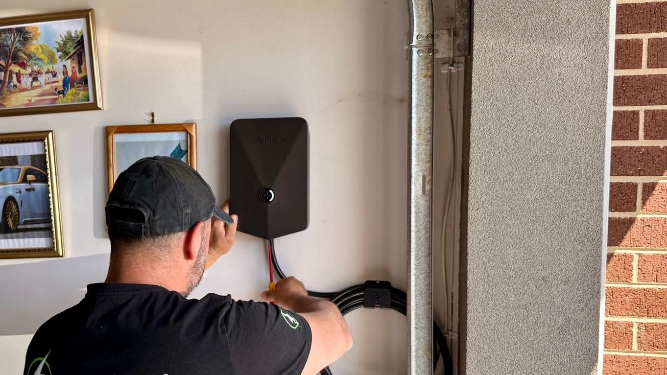 Yiannis mounting a black EV charger on a garage wall