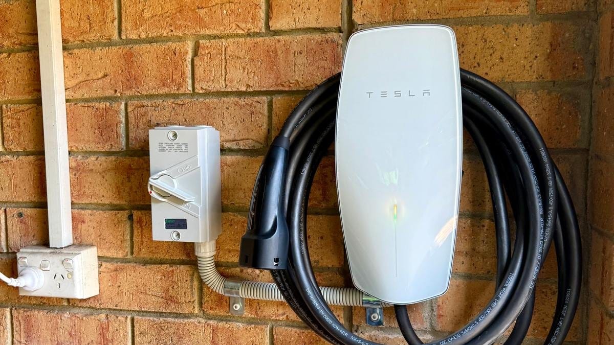 Tesla wall connector with its cable coiled on a brick wall beside an isolator