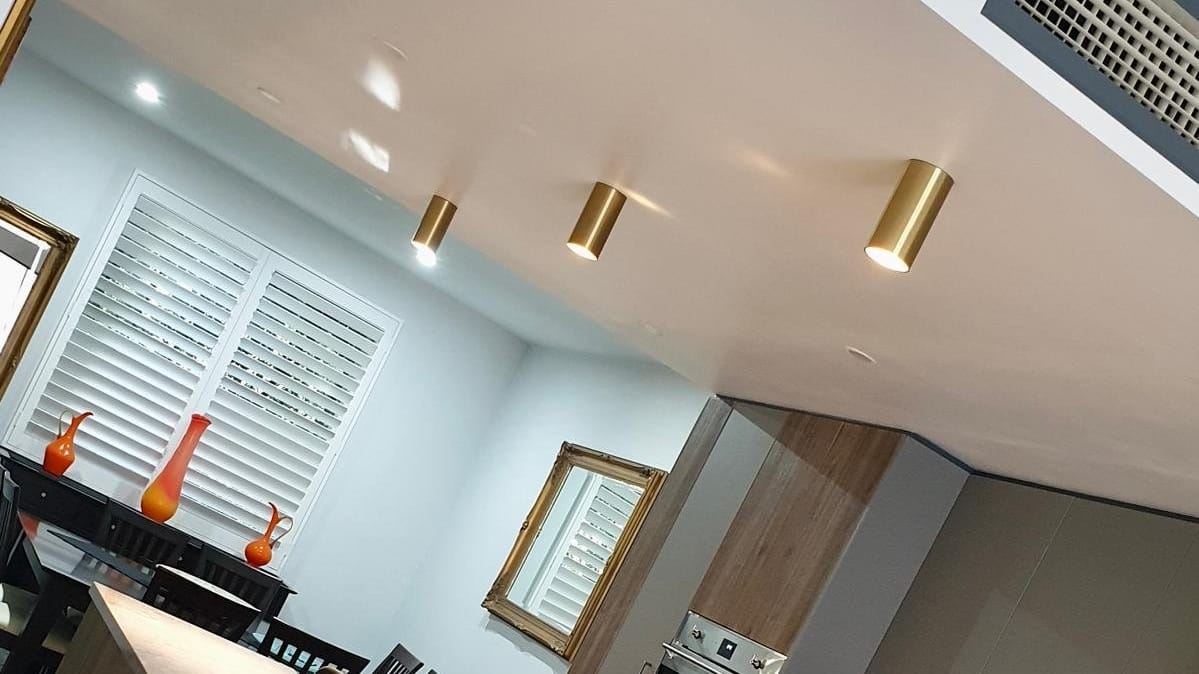 Gold cylinder downlights on the ceiling above a kitchen and dining area