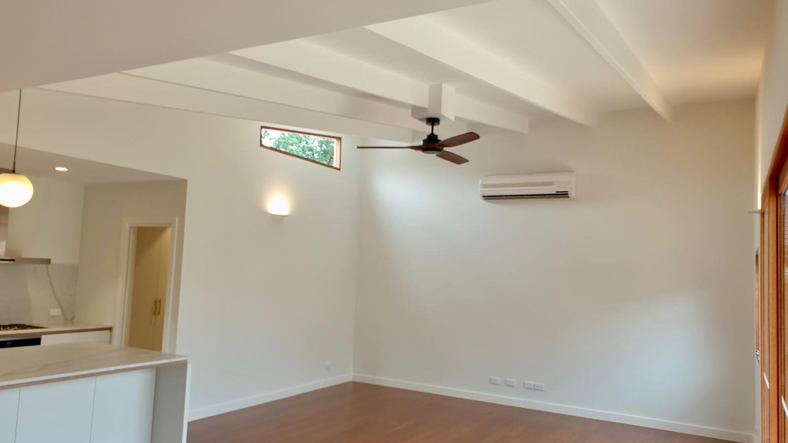 Open-plan living area with a ceiling fan, a wall light, a split system and timber floors