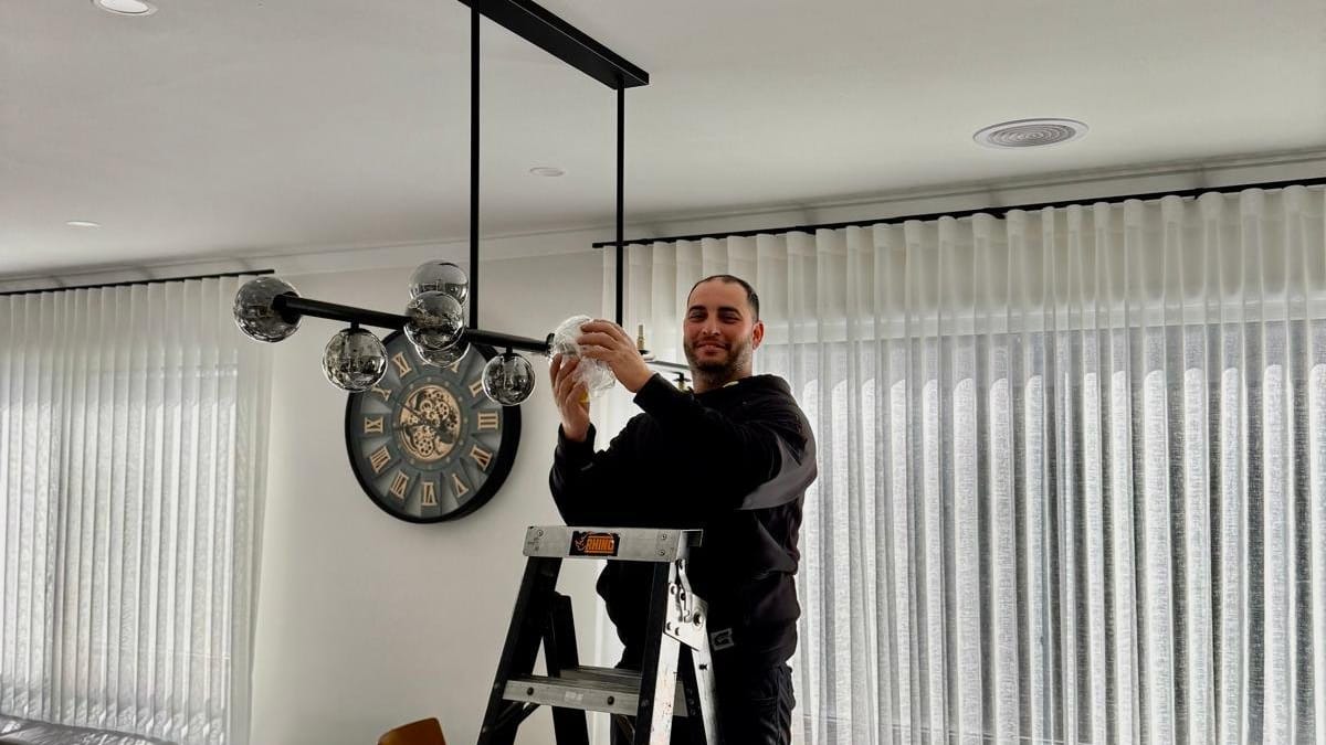 Yiannis on a stepladder fitting a multi-globe pendant light in a dining room