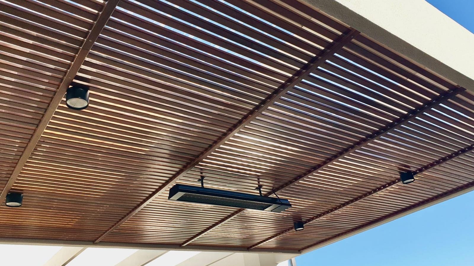 Timber-slat pergola fitted with an outdoor strip heater and small downlights