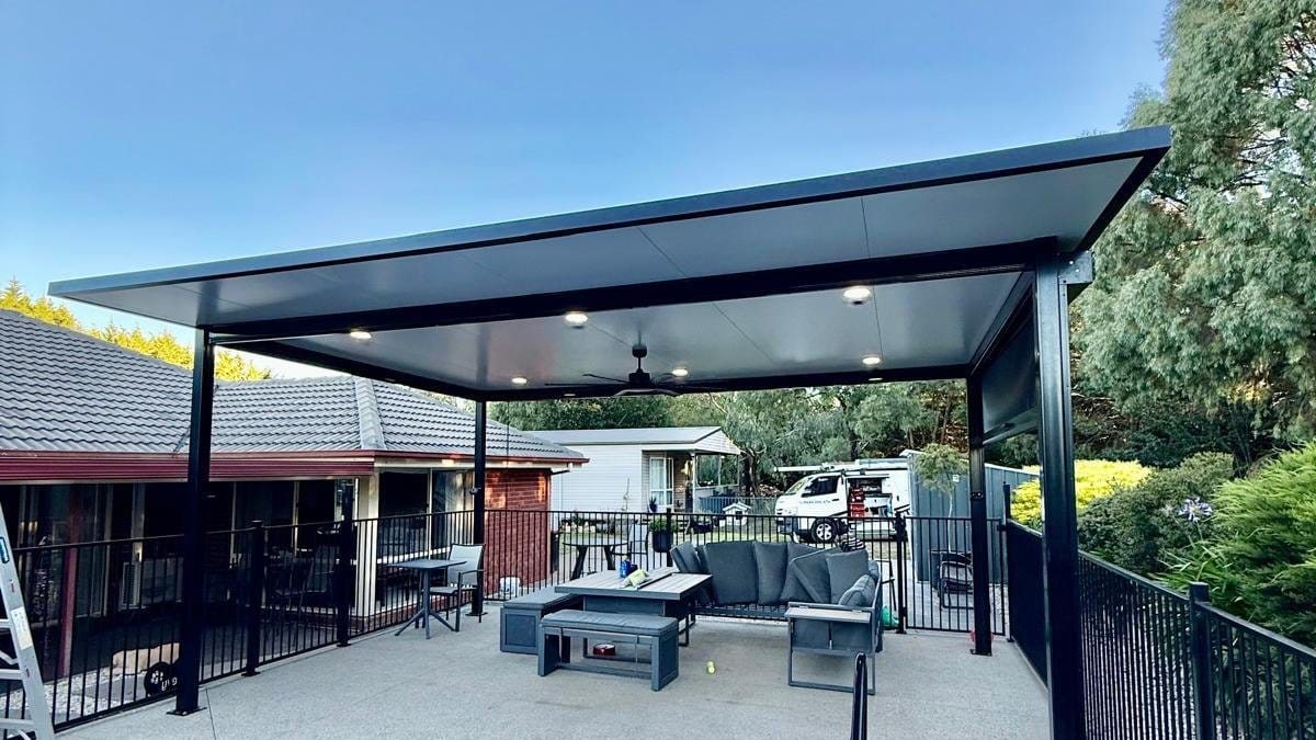 Outdoor pavilion with downlights and a ceiling fan behind a fenced backyard