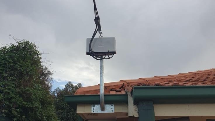 Overhead power line connected to a galvanised mast above a tiled roof