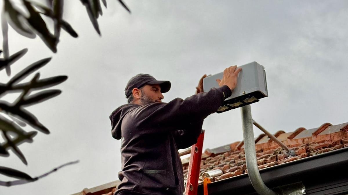 Yiannis on a ladder at the gutter line, working on a connection box on a galvanised mast