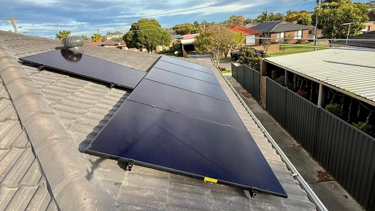 Black solar panels on a grey tiled roof with suburban houses behind