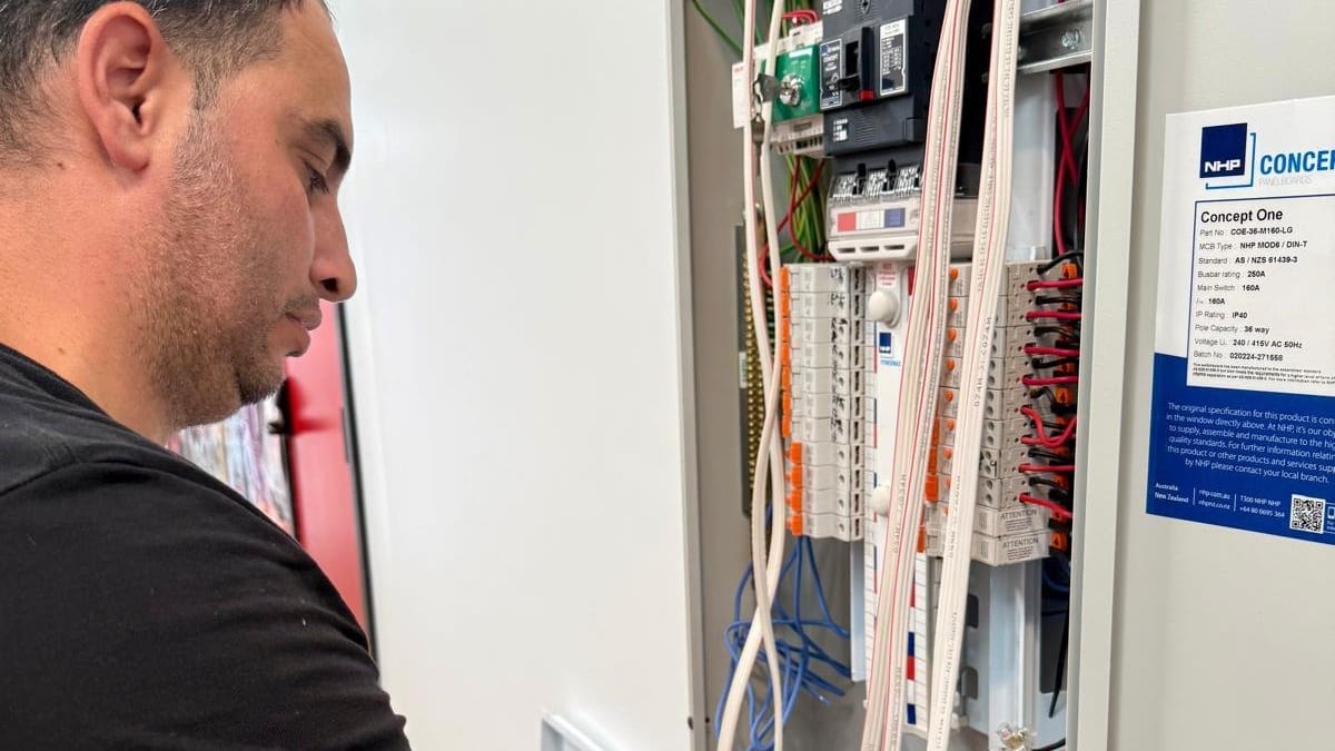 Yiannis working inside an open distribution board full of breakers and cabling