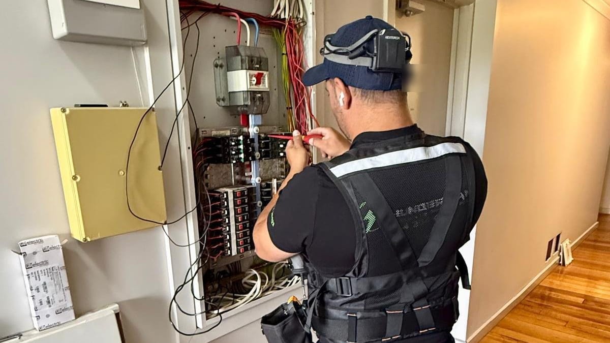 Yiannis in a work vest wiring an open distribution board in a hallway