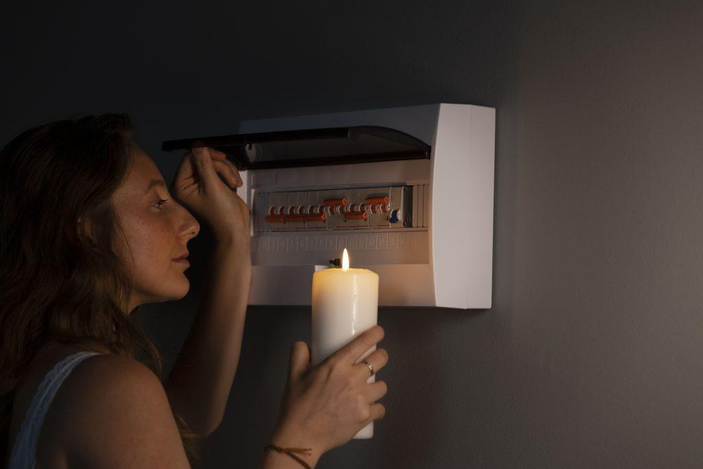 Woman checking fuse box by candlelight during power outage in Melbourne