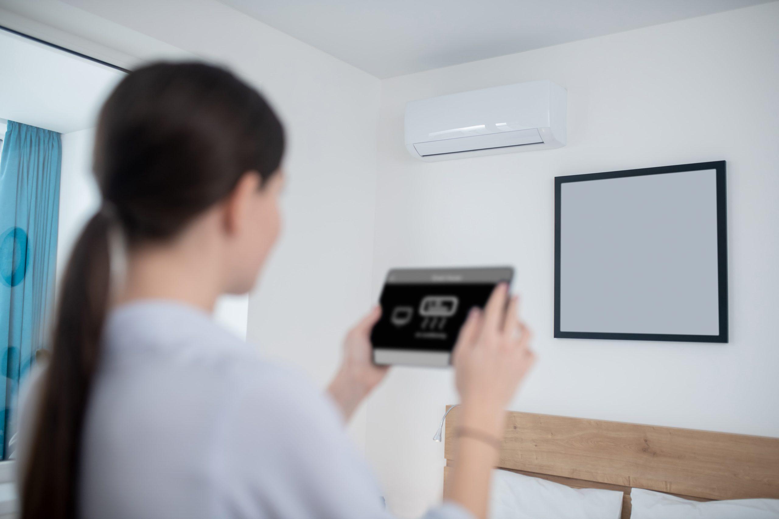 Woman controlling air conditioner with a tablet in a modern bedroom.